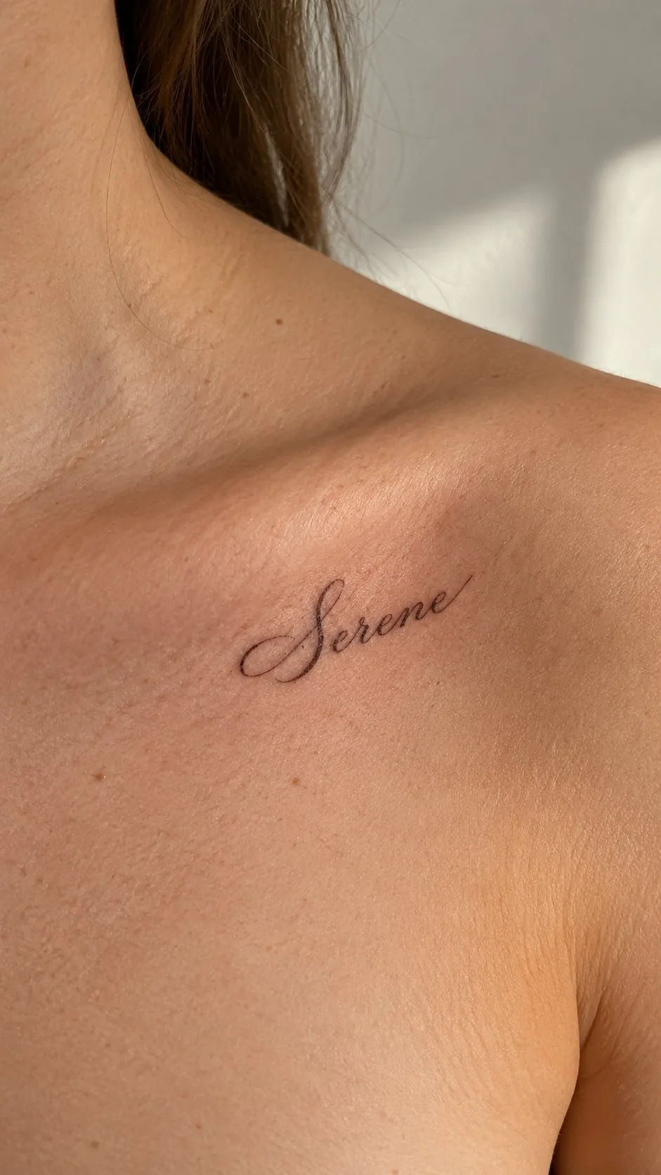 Fine script tattoo reading Serene on the collarbone