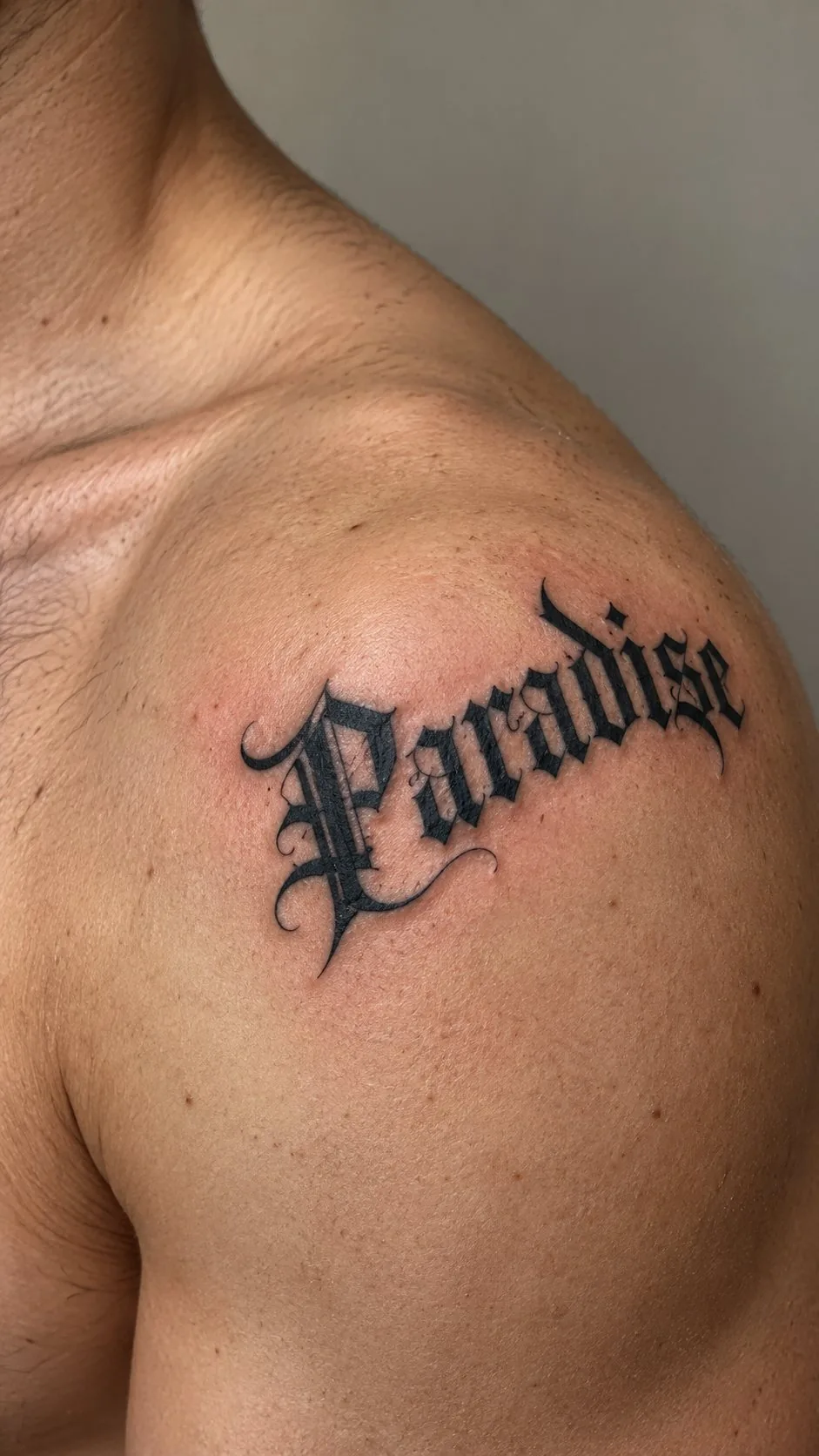Blackletter tattoo reading Paradise on the shoulder